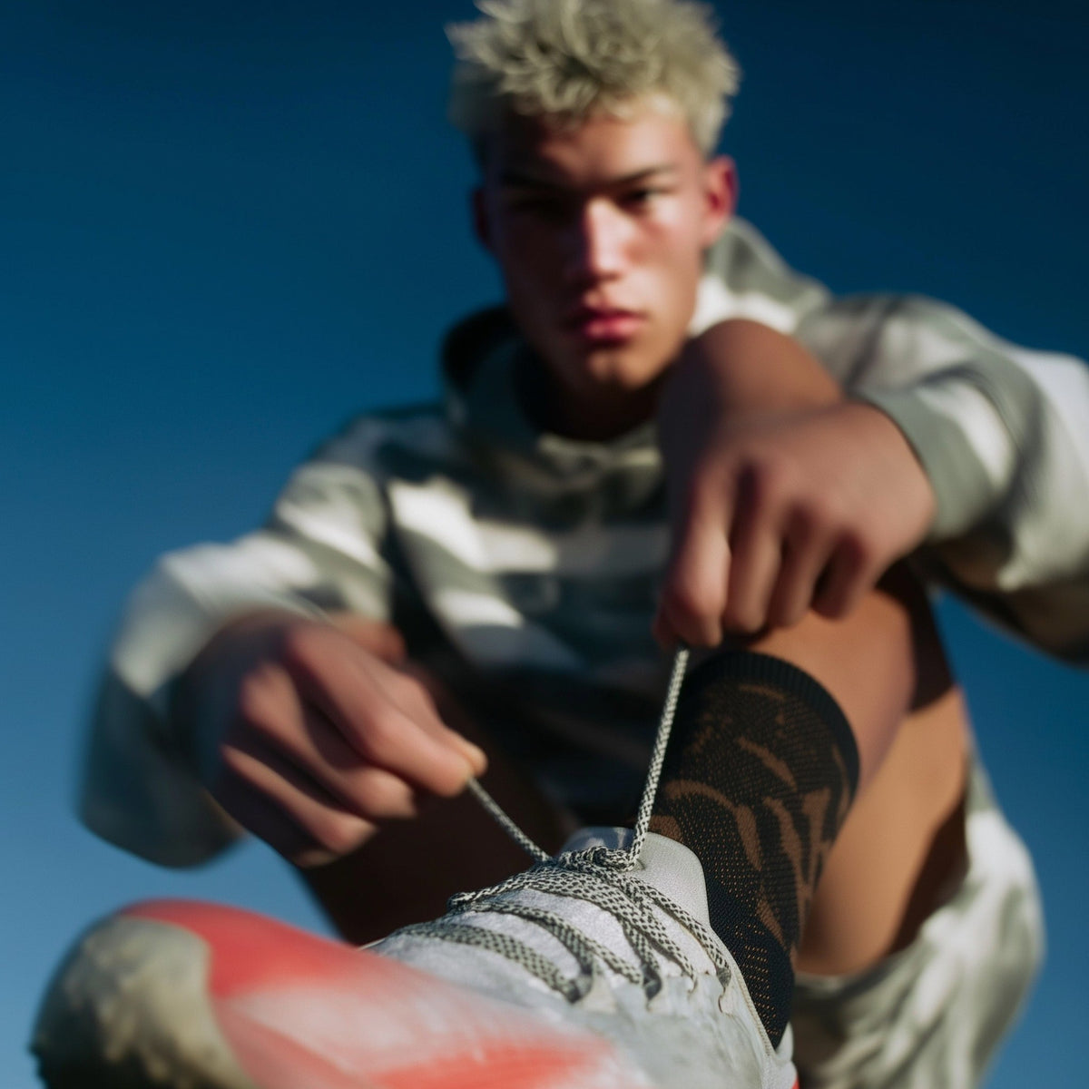 Person tying shoelaces against a clear blue sky (Beige)