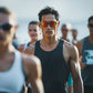 Man wearing sunglasses and athletic gear with a group of people in the background (Orange)